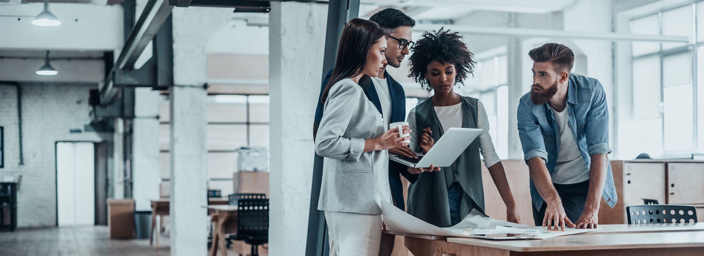 Four people standing around a table in an office, discussing documents.